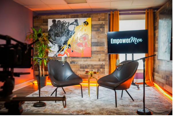EmpowerMen talk-show set with two chairs and orange curtains